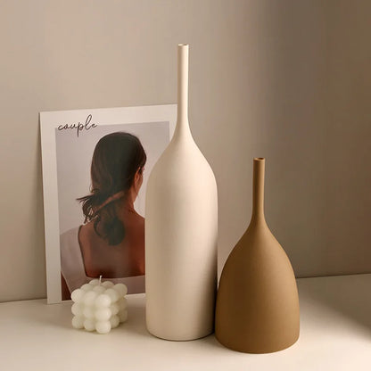 Two ceramic vases, one white and one brown, on a surface with a minimalistic poster in the background.