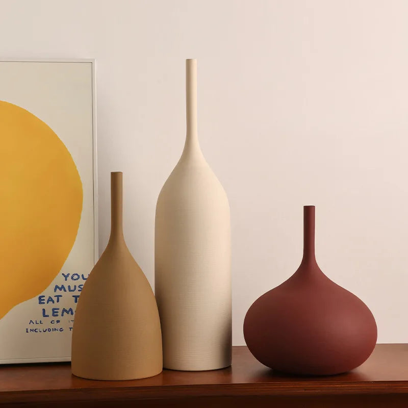 Three ceramic vases of different colors on a wooden surface with a poster in the background.