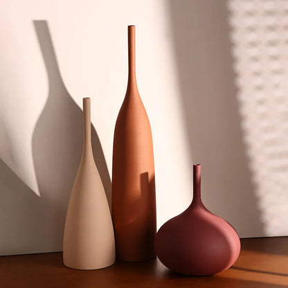 Three ceramic vases of different shapes and colors on a wooden surface with a neutral background